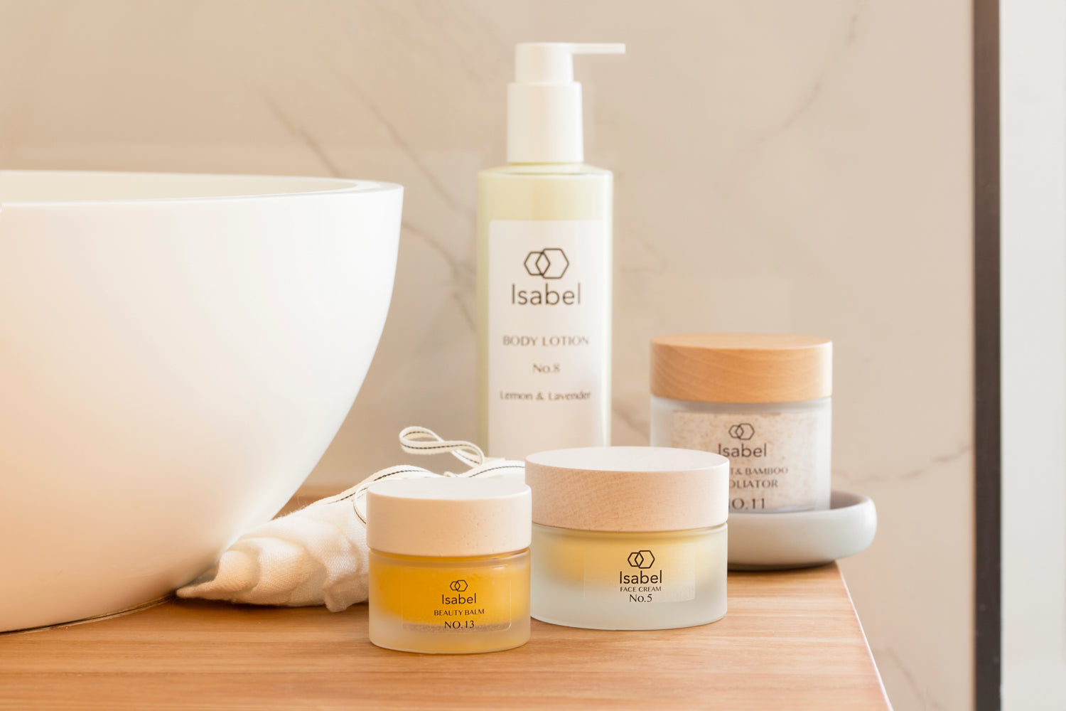 Selection Isabel skincare products grouped next to a white stone hand basin, Beauty balm, body lotion, exfoliator and No.5 face cream.